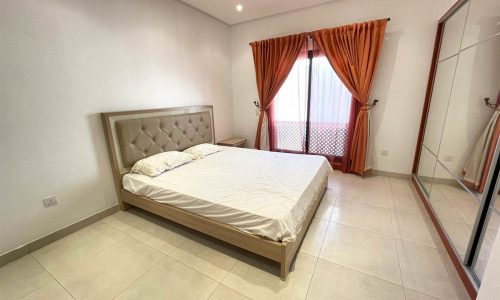 A stunning bedroom with a bed, dresser, and mirror in a secure apartment for rent in Busaiteen.