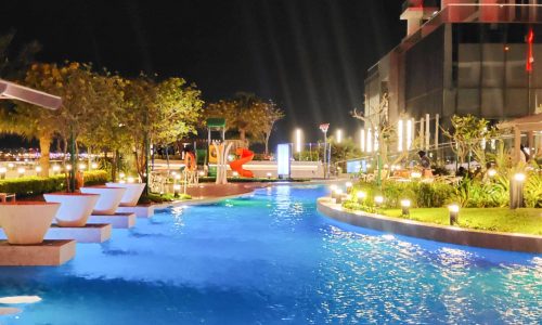 A spacious swimming pool with lounge chairs at night.