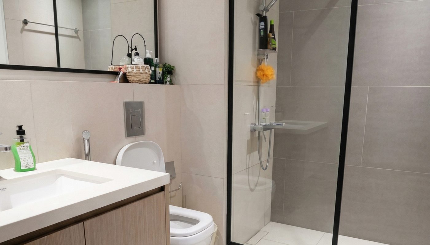 Modern bathroom with a glass shower enclosure, wall-mounted toilet, large mirror, sink with wooden cabinet, and towel rack on beige tiled walls and floor.