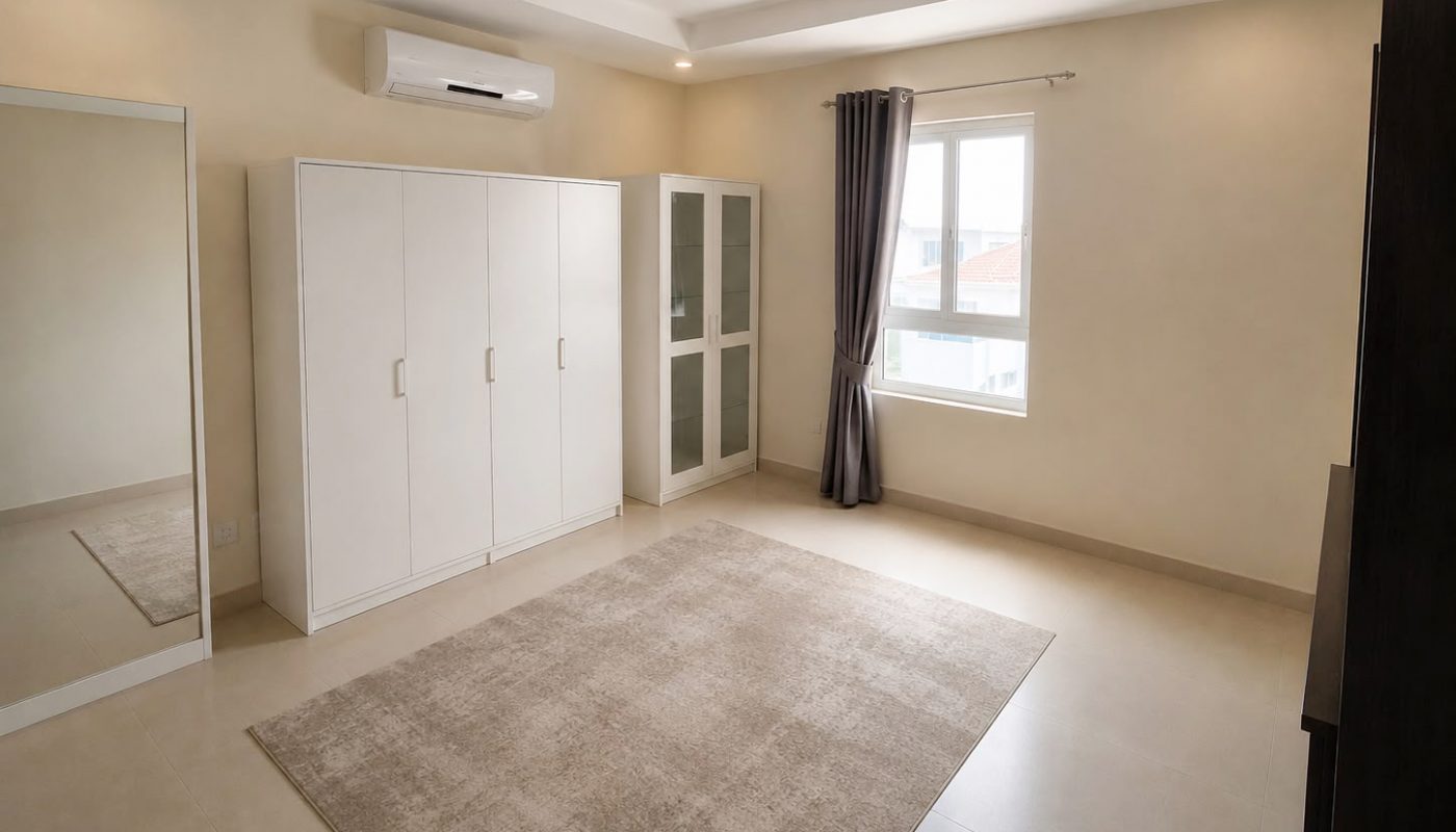 Minimalist bedroom with a large beige rug, white wardrobe, floor mirror, curtained window, and an air conditioner mounted above the wardrobe.