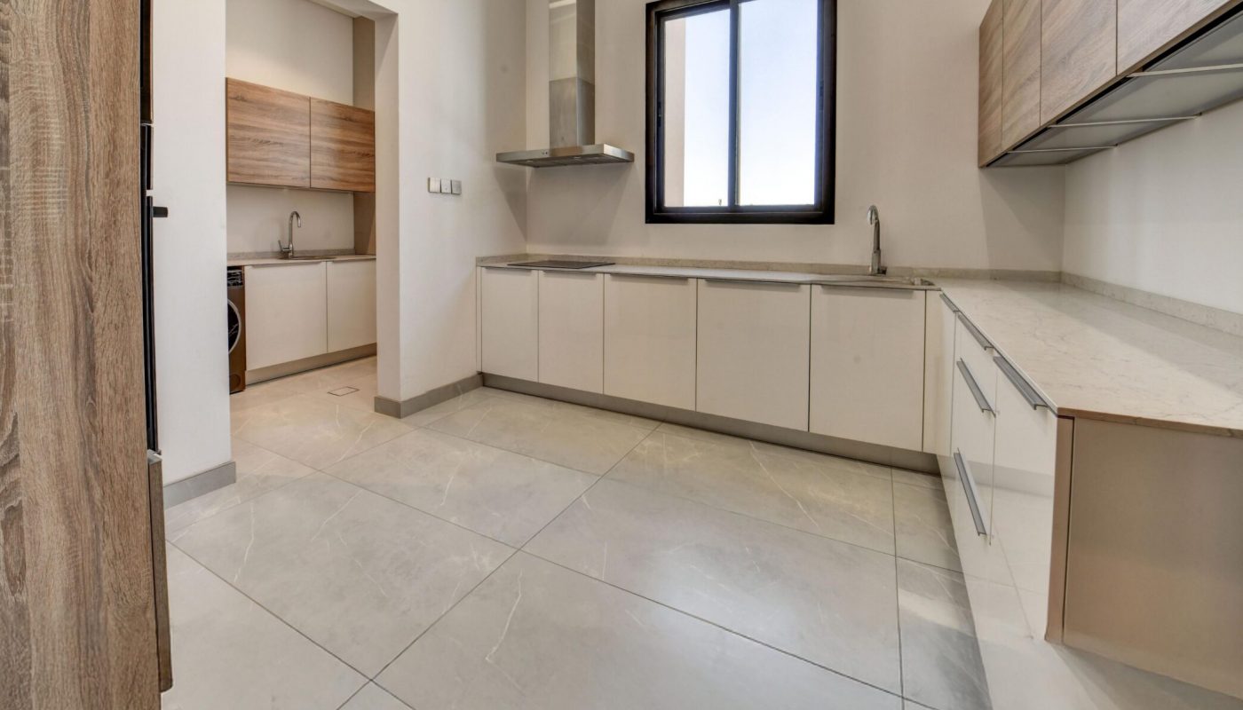 Modern kitchen with white cabinets, light wood accents, tile flooring, window, and a separate pantry or laundry area visible through an open doorway.
