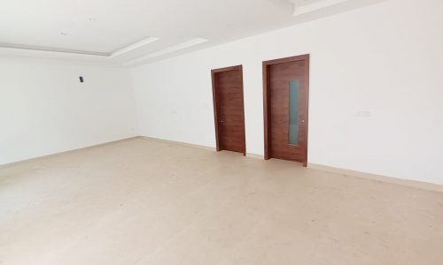 Empty room with wooden doors and white walls in a 4BR Villa for Sale in Bani Jamra.