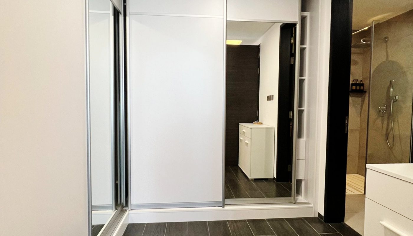 Modern bathroom with dark wood flooring, large mirrors, sliding closet doors, glass shower enclosure, and white cabinetry.