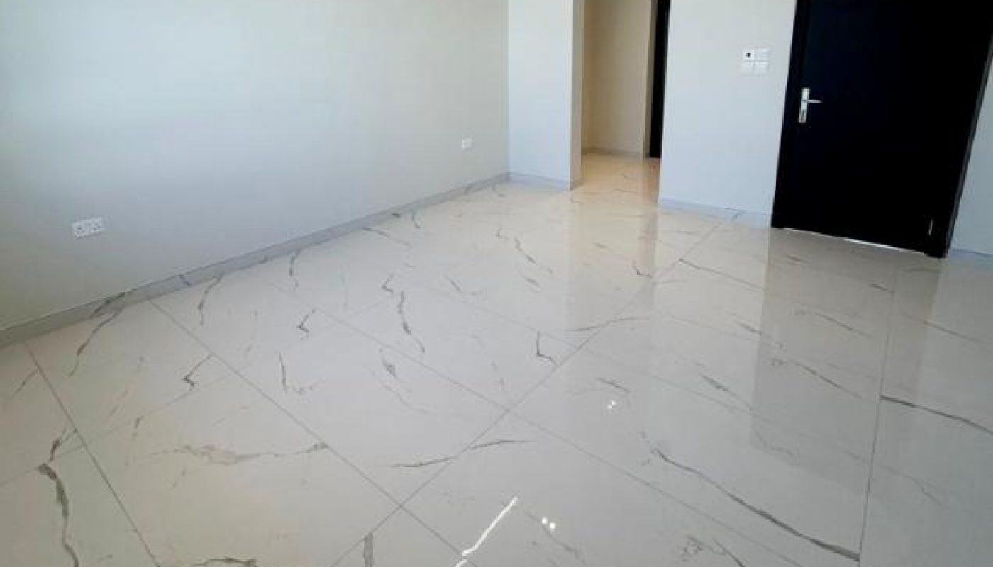 Empty modern room with large white marble floor tiles, white walls, a black door, and recessed ceiling lights.