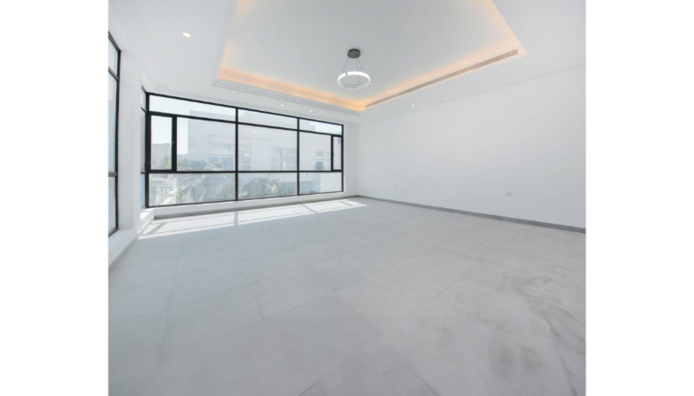 Spacious empty room with large floor-to-ceiling windows, white walls, gray tile flooring, and a modern ceiling light fixture.