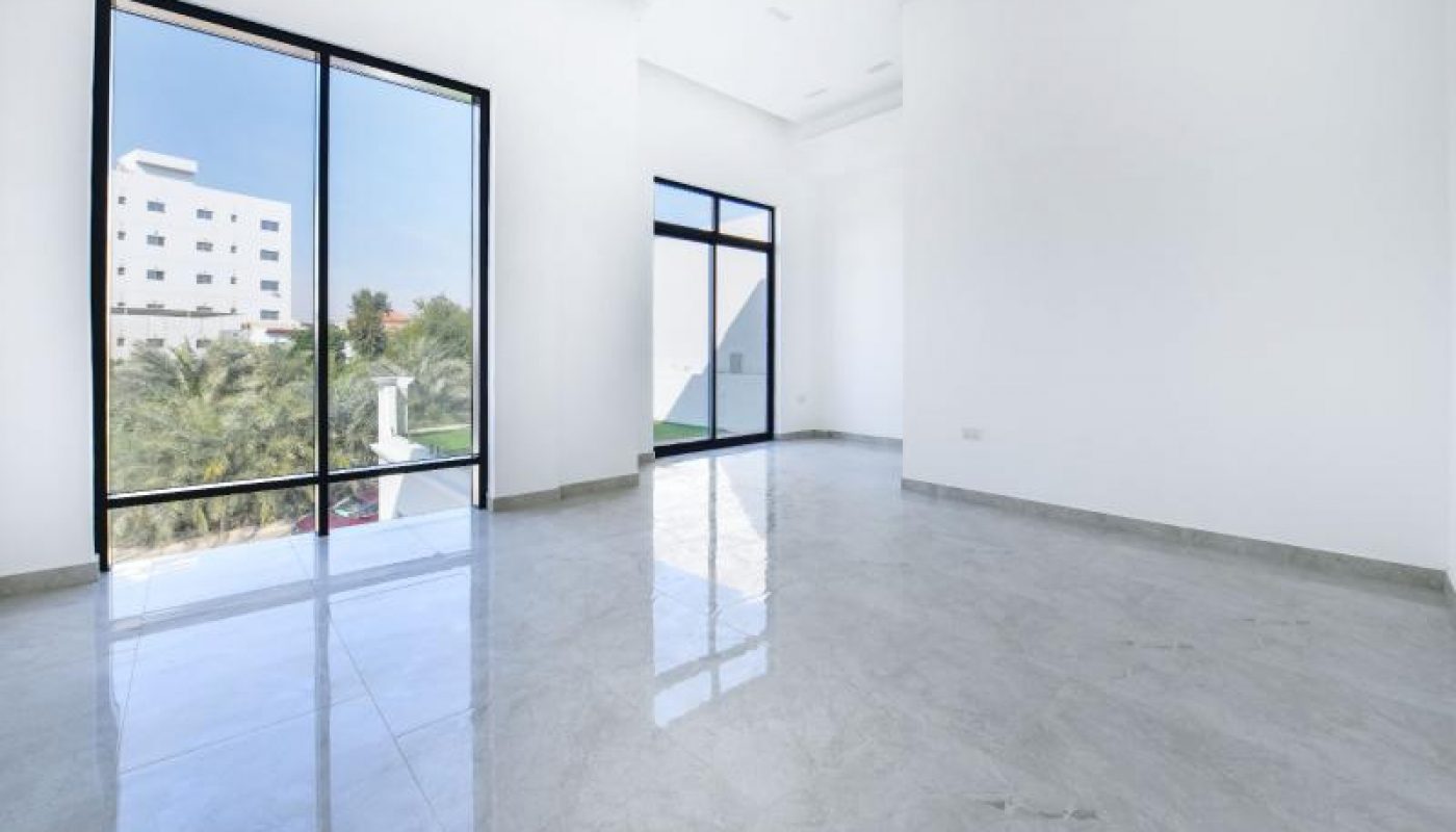 Empty, modern room with large glass windows, white walls, marble floor, and a circular ceiling light. Trees and a building are visible outside.