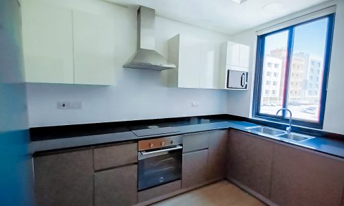 An empty kitchen with a stove and sink in a residential building for sale in Janabiyah.