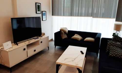 A modern living room with a couch, coffee table and tv in a luxury apartment for sale in Juffair.