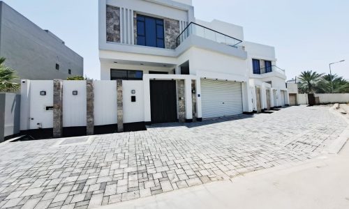 Modern two-story white villa with a balcony, large windows, and a garage, situated in a peaceful area of Saar.