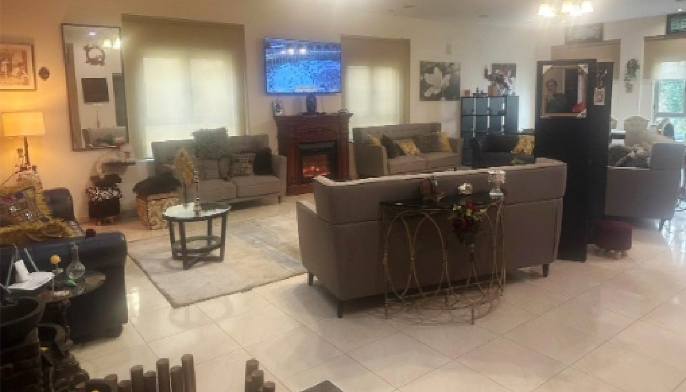 Spacious living room with multiple gray sofas, a TV mounted above a fireplace, various lamps, wall art, and decorative items on tables and shelves.