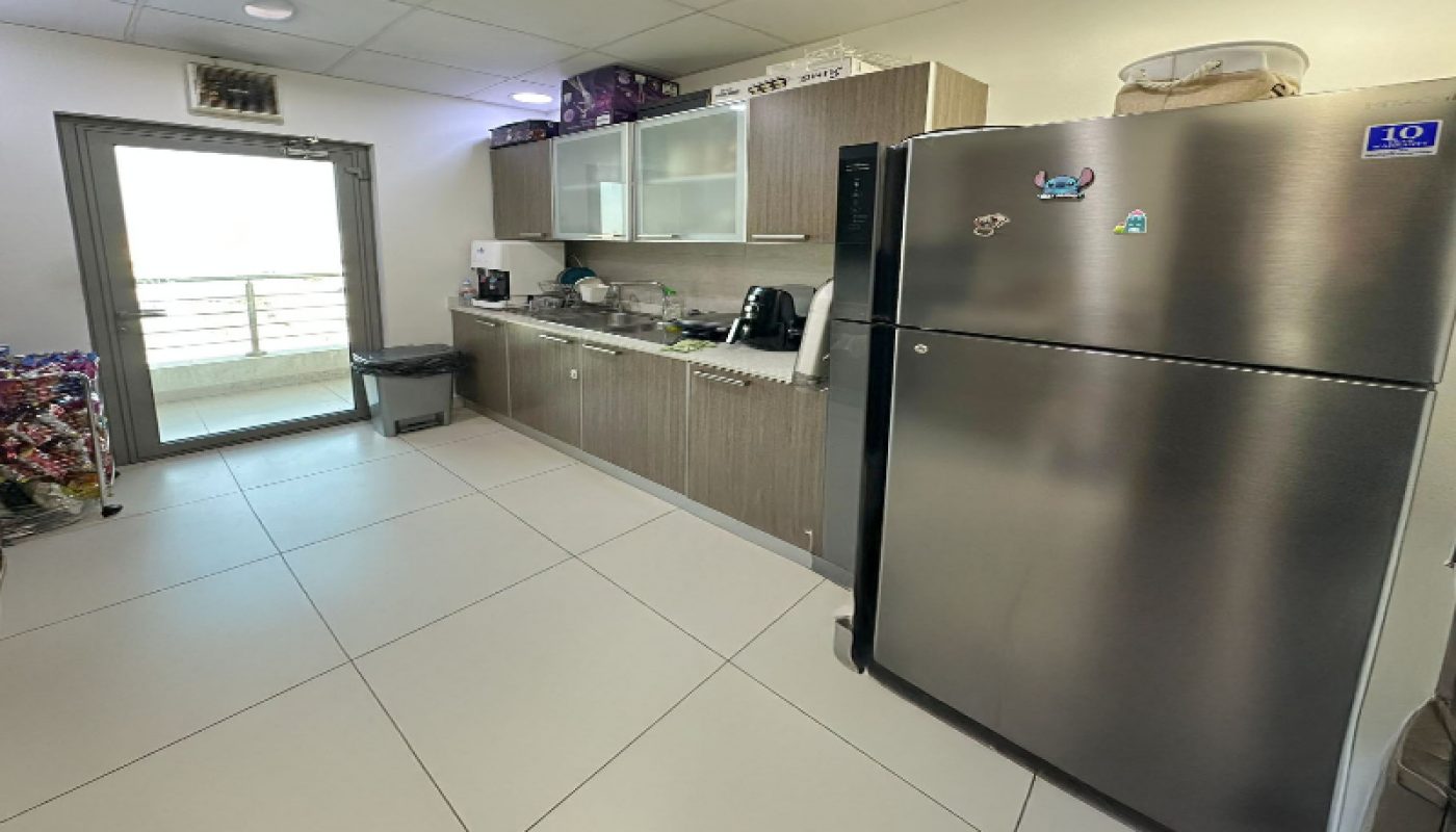 Modern kitchen with stainless steel refrigerator, wooden cabinets, small appliances on the counter, and a glass door leading to a balcony.