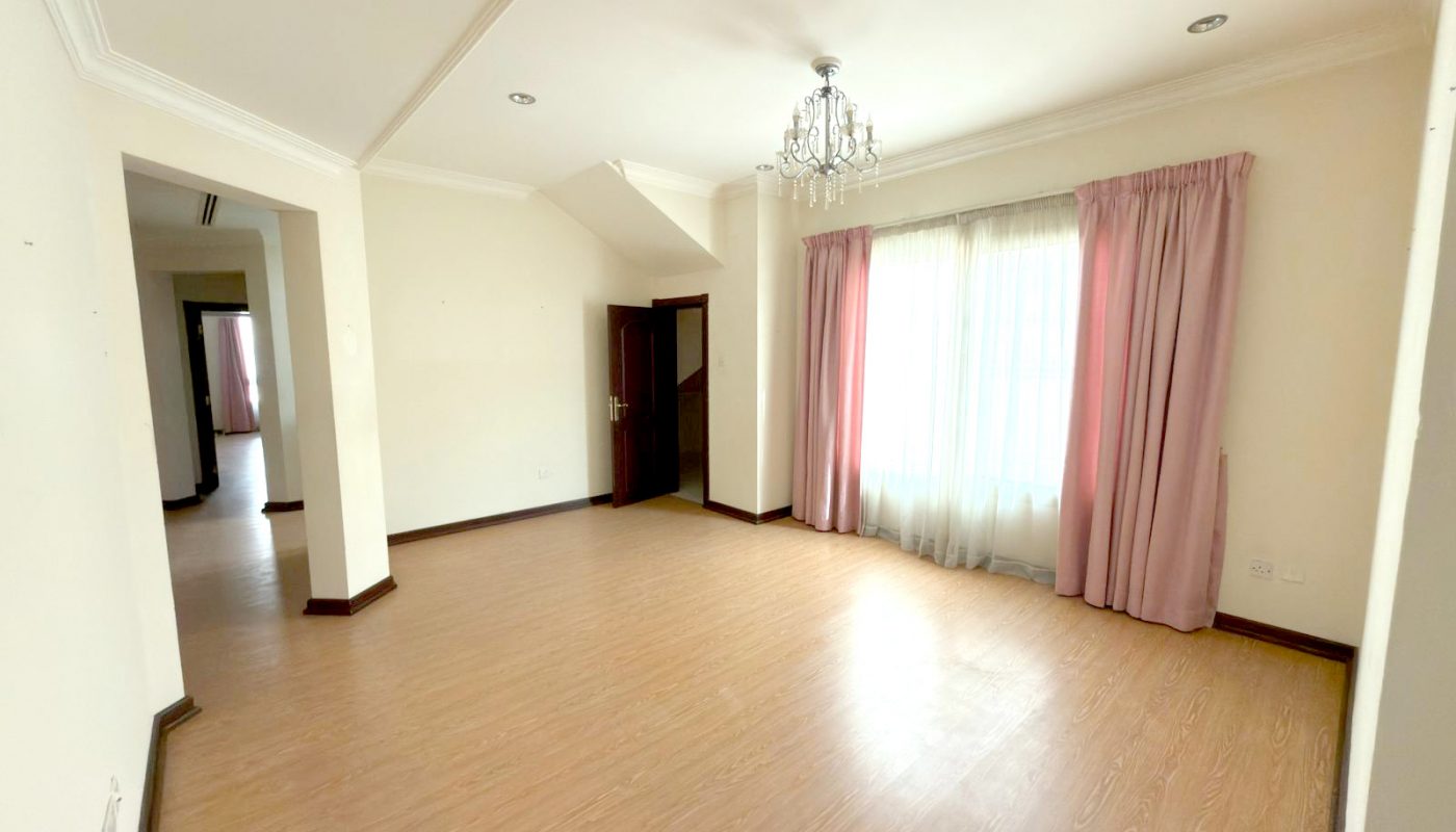 Empty living room with light wood flooring, cream walls, a large window with pink curtains, a chandelier, and an open doorway leading to another room.