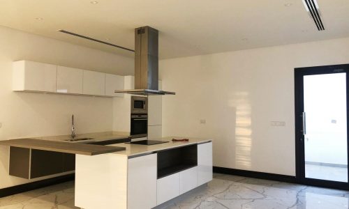 A luxury private 4-bedroom villa for rent in Saar with a white kitchen featuring marble counter tops and stainless steel appliances.