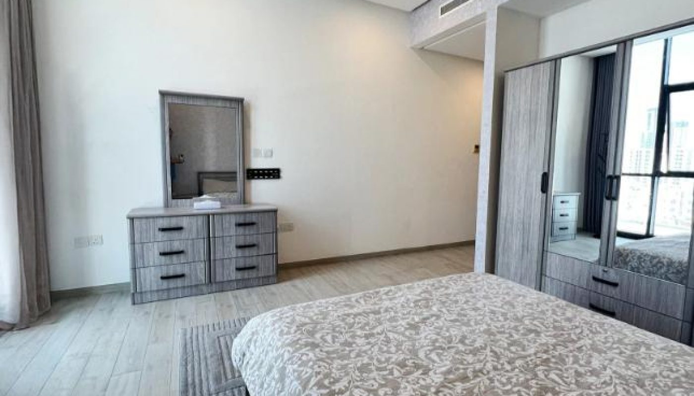 Modern bedroom with a patterned bedspread, light wood flooring, a dresser with a mirror, large windows, and mirrored wardrobe doors.