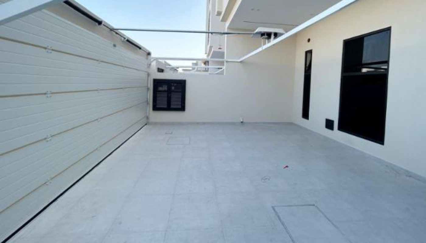 A clean, empty outdoor patio with light gray tiles beside a white building and a closed garage door under a clear sky.