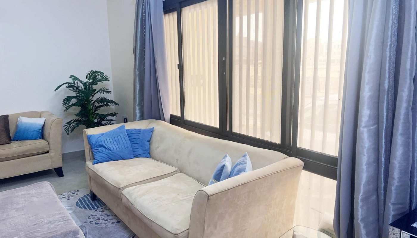 A cozy living room with a couch and TV in a 2BR apartment for sale in Busaiteen.