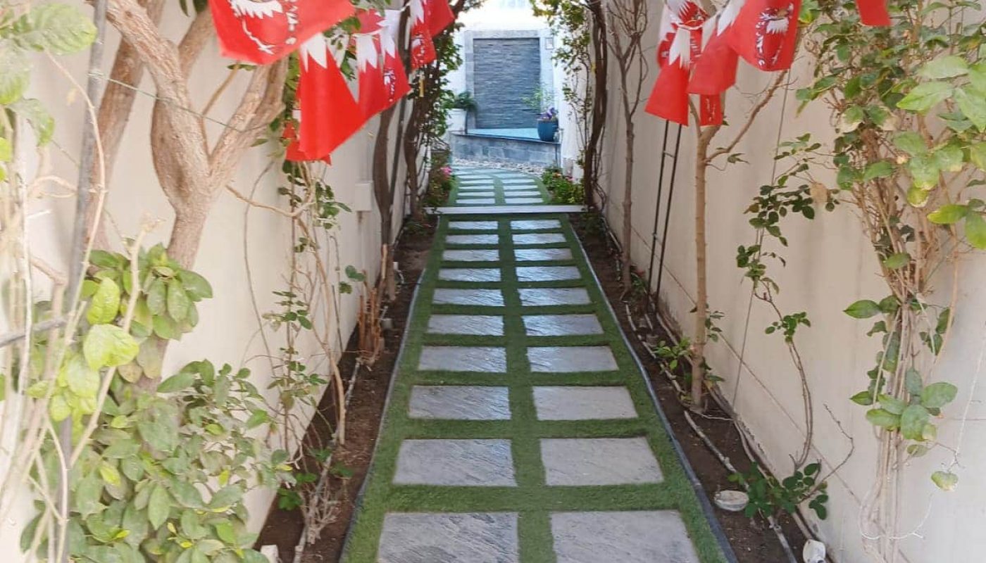 A narrow walkway lined with trees and grass, decorated with red and white flags overhead.