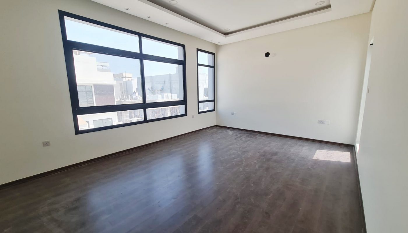 Empty room with large windows, white walls, dark wood flooring, and a recessed ceiling. Natural light enters from the windows, and no furniture or decor is present.