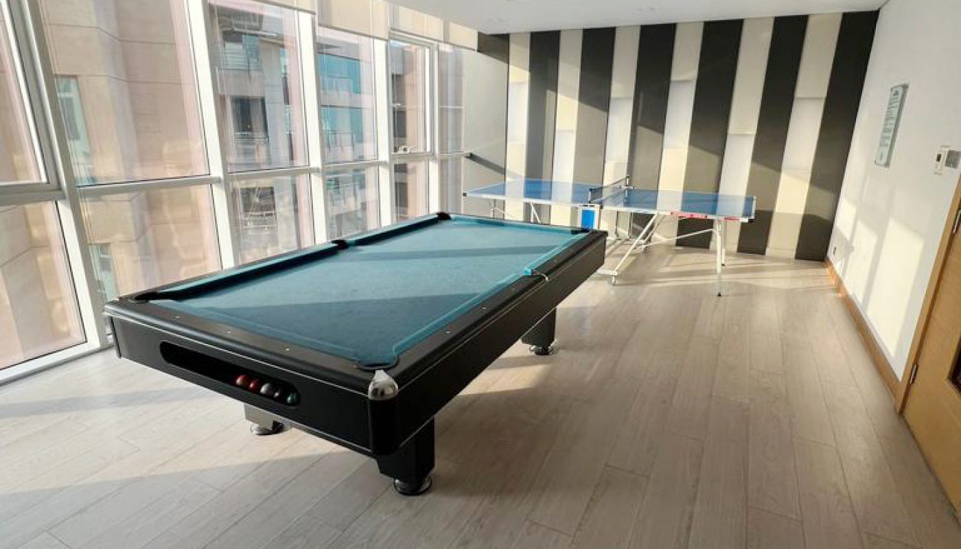 A modern game room with a pool table and a ping pong table, large windows along one wall, and striped wallpaper on the far wall.