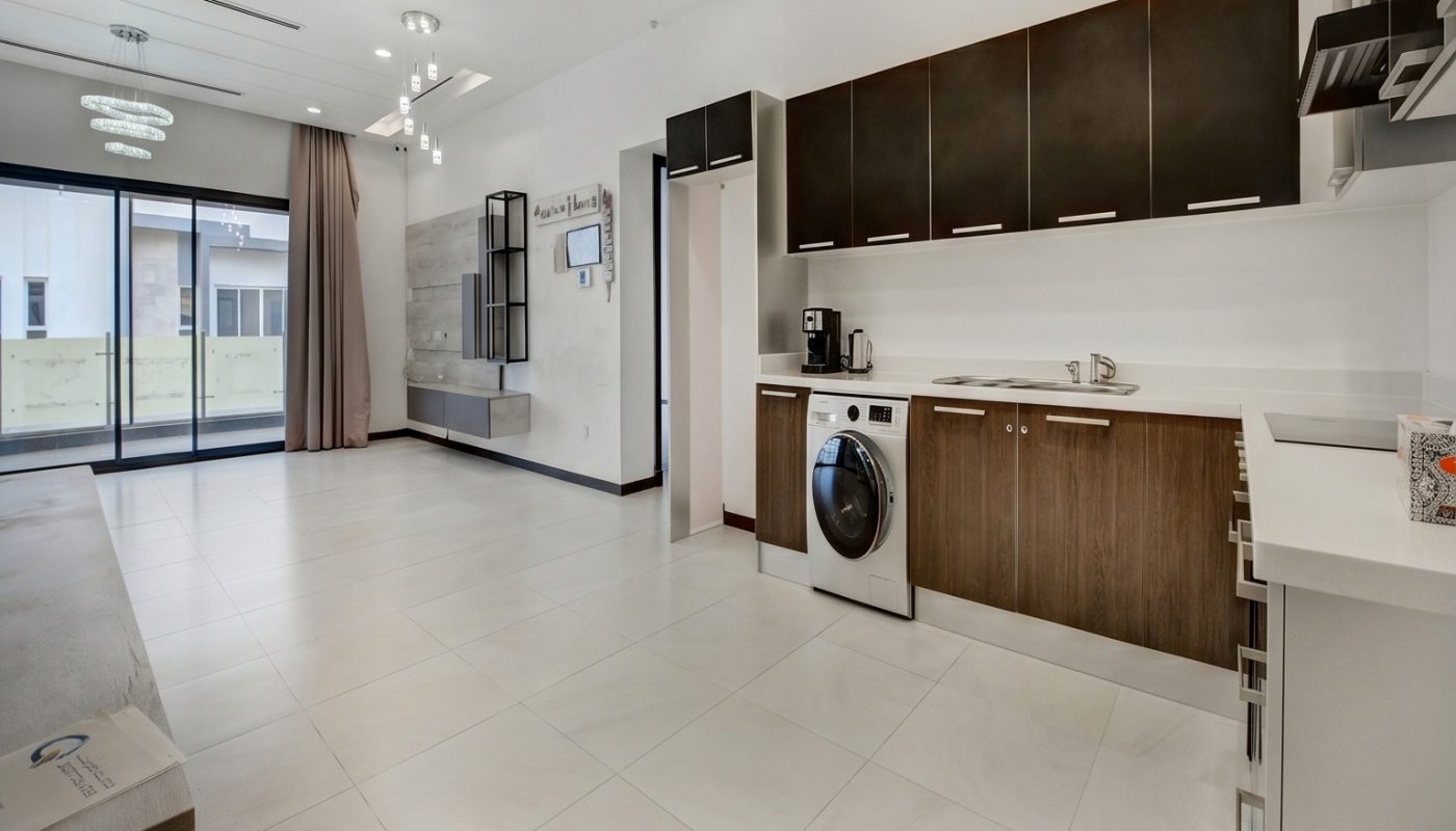 Modern open-plan kitchen and living area with tile flooring, built-in appliances, dark and light cabinetry, large window, and washing machine in kitchen.