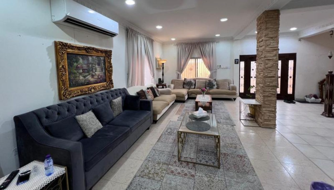Spacious living room with multiple sofas, a large framed painting, coffee tables, stone pillar, tile flooring, and large windows with curtains.