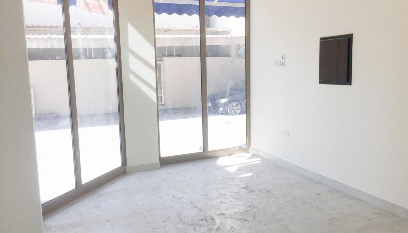 Empty room with large windows, white walls, and tiled floor. Sunlight streams in, highlighting some dust on the floor. A flat rectangular panel is mounted on the right wall.