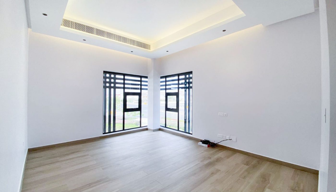 Empty room with light wood flooring, white walls, two windows with black horizontal blinds, and recessed ceiling lights. Electrical outlets and a device are visible on the right wall.