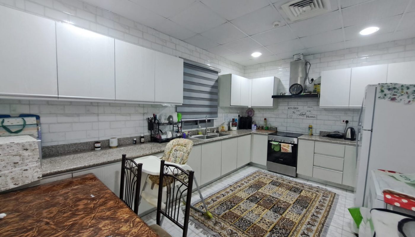 A furnished kitchen with white cabinets and a rug on the floor.