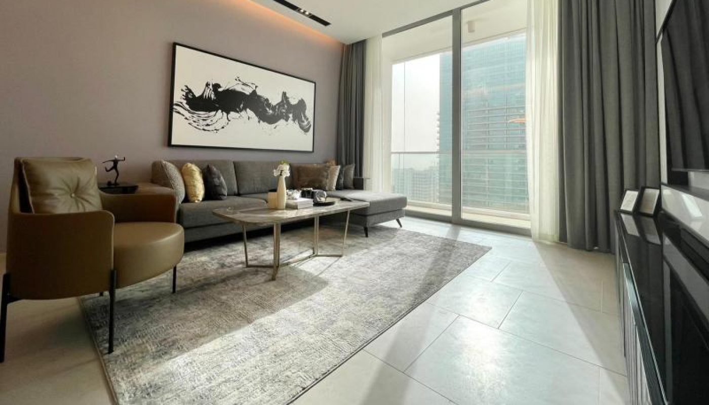 Modern living room with a gray sofa, coffee table, armchair, large rug, abstract wall art, floor-to-ceiling windows, and cityscape view.