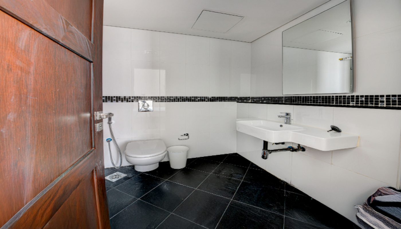 A modern bathroom with black tiled floor, white walls, a wall-mounted sink, a toilet, a bidet spray, and a large mirror above the sink.