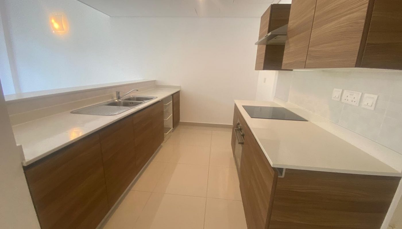 Modern kitchen with wood cabinets, white countertops, stainless steel sink, electric stovetop, oven, and beige tiled floor.