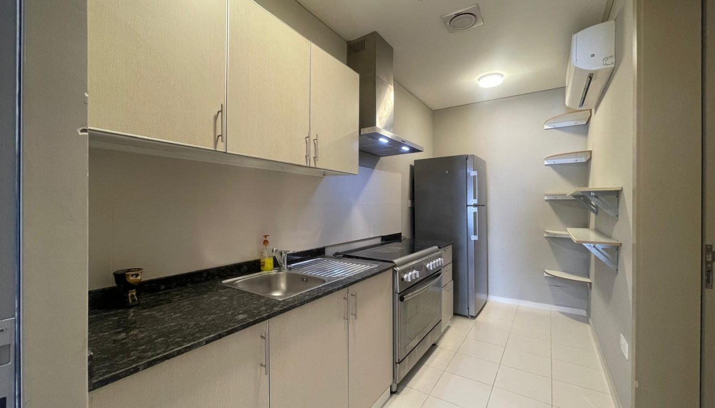 Modern kitchen with light-colored cabinets, black countertop, stainless steel appliances, open shelving on the right, and white tiled floor.