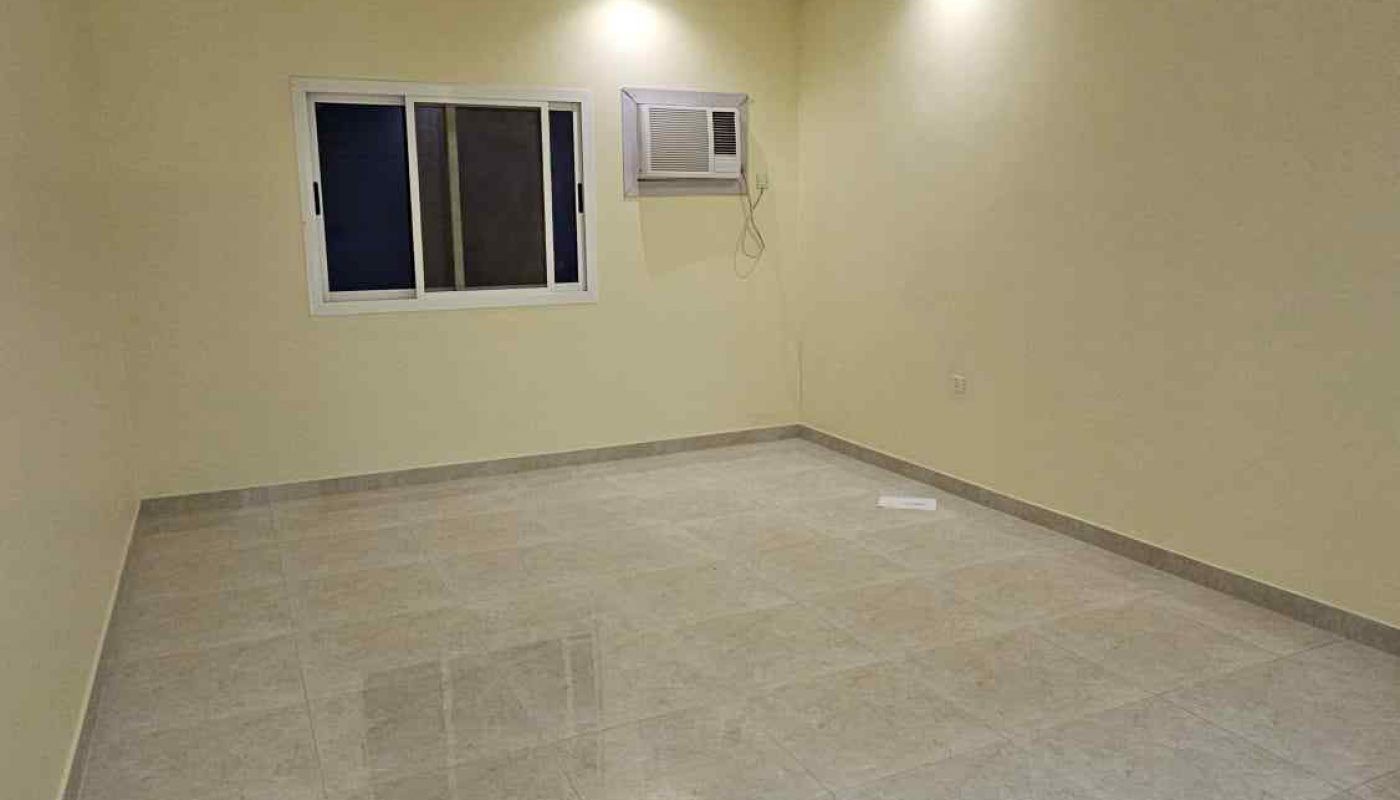 Empty room with cream-colored walls, tiled floor, ceiling lights, a ceiling fan, a window, and a wall-mounted air conditioning unit.