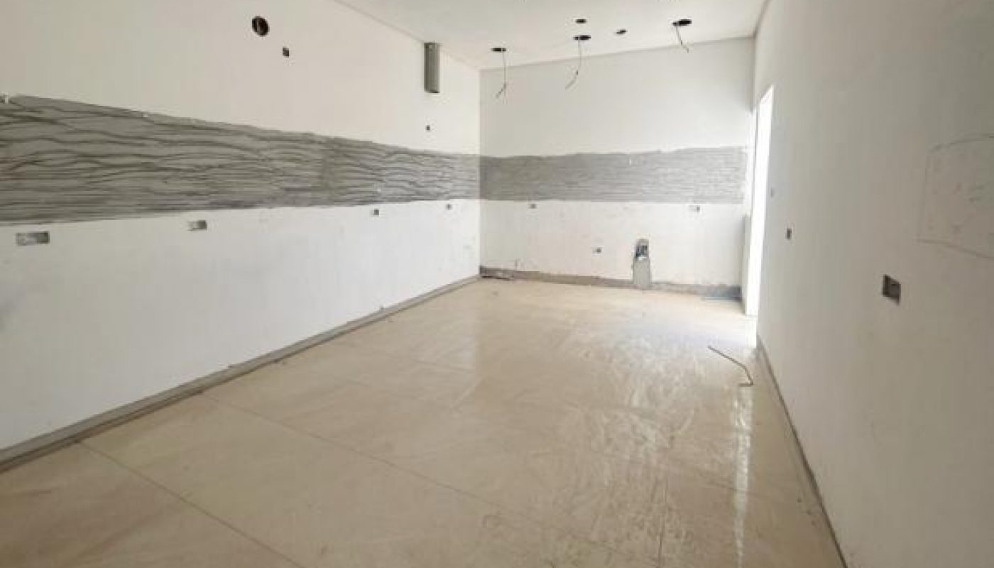 Unfinished room with tiled floor, exposed wiring on the ceiling, and unpainted wall sections, likely under construction or renovation.