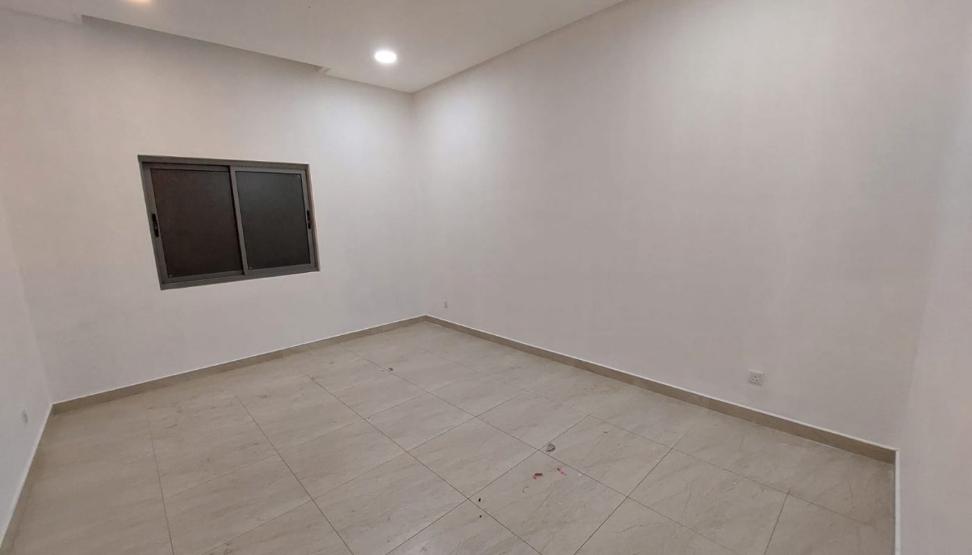 Empty room with tiled floor, white walls, a single window with black frame, and ceiling lights.