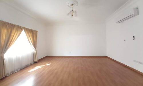 Empty room with polished wooden floor, white walls, a ceiling fan, an air conditioner, and a large window with gold curtains.