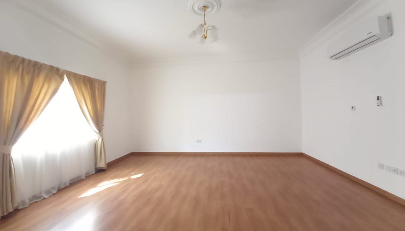 Empty room with polished wooden floor, white walls, a ceiling fan, an air conditioner, and a large window with gold curtains.
