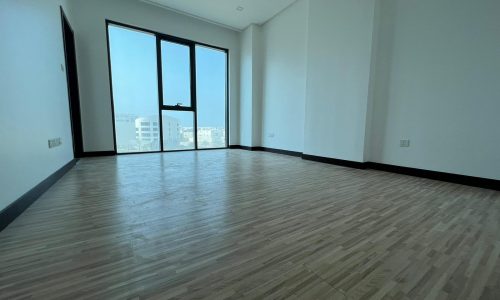 An empty apartment with hardwood floors and large windows.