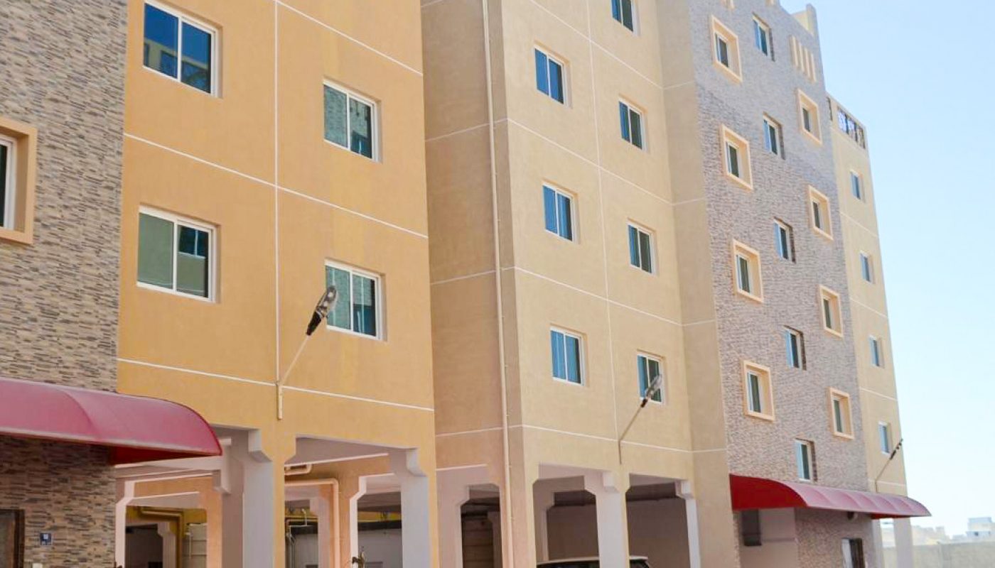 Four-story residential apartment buildings with yellow and beige exteriors, red awnings, and ground-level parking under the buildings.