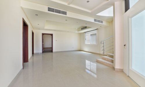 Luxury Villa in the Janbiyah area: Spacious, semi-furnished modern interior with high ceiling, large windows, and glossy tiled floor. Stairs on the right lead to another level.