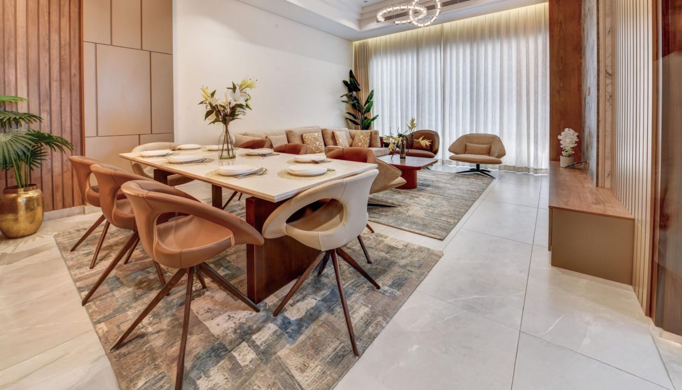 Modern dining and living area with a large dining table, beige chairs, patterned rug, contemporary lighting fixtures, and floor-to-ceiling curtains.