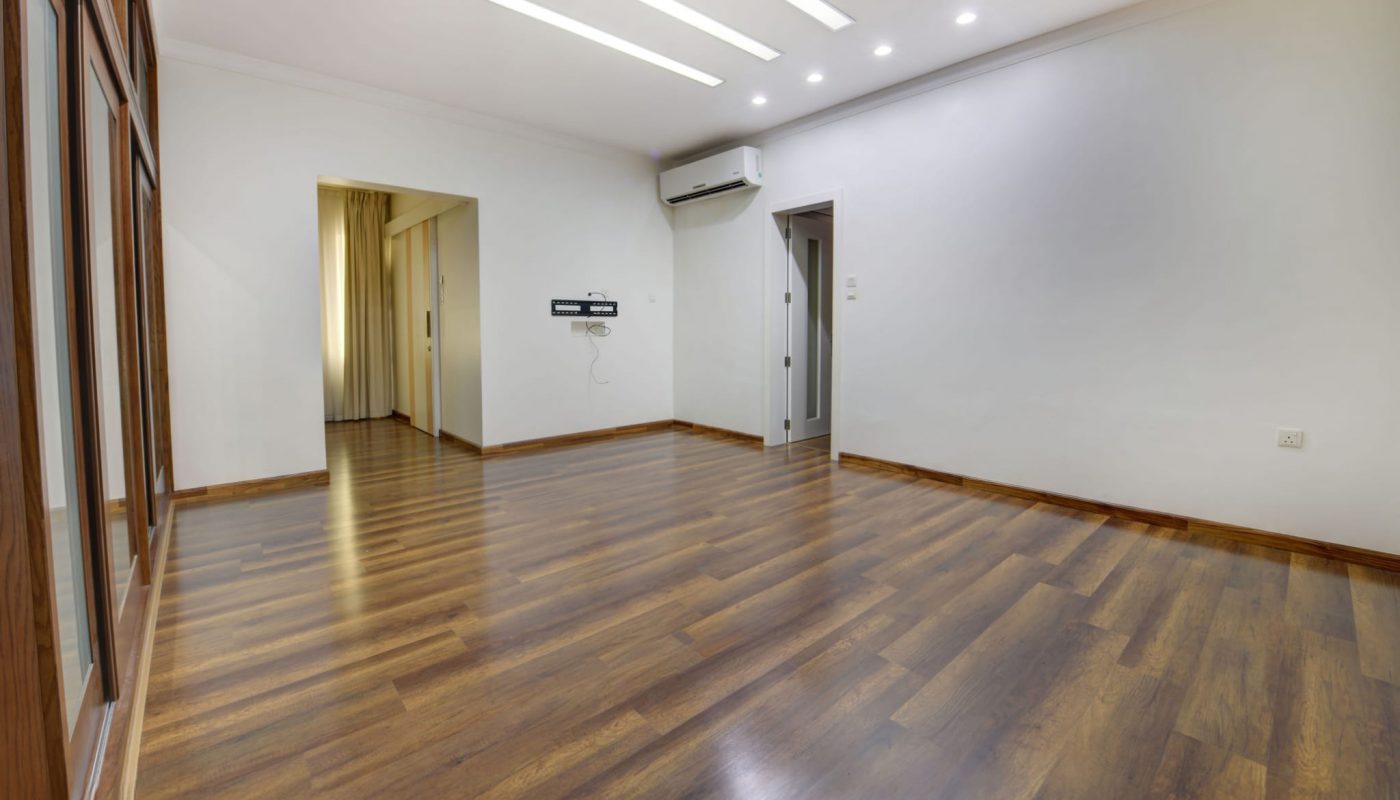 Empty room with wooden flooring, white walls, ceiling lights, large windows on one side, and doors leading to other rooms.