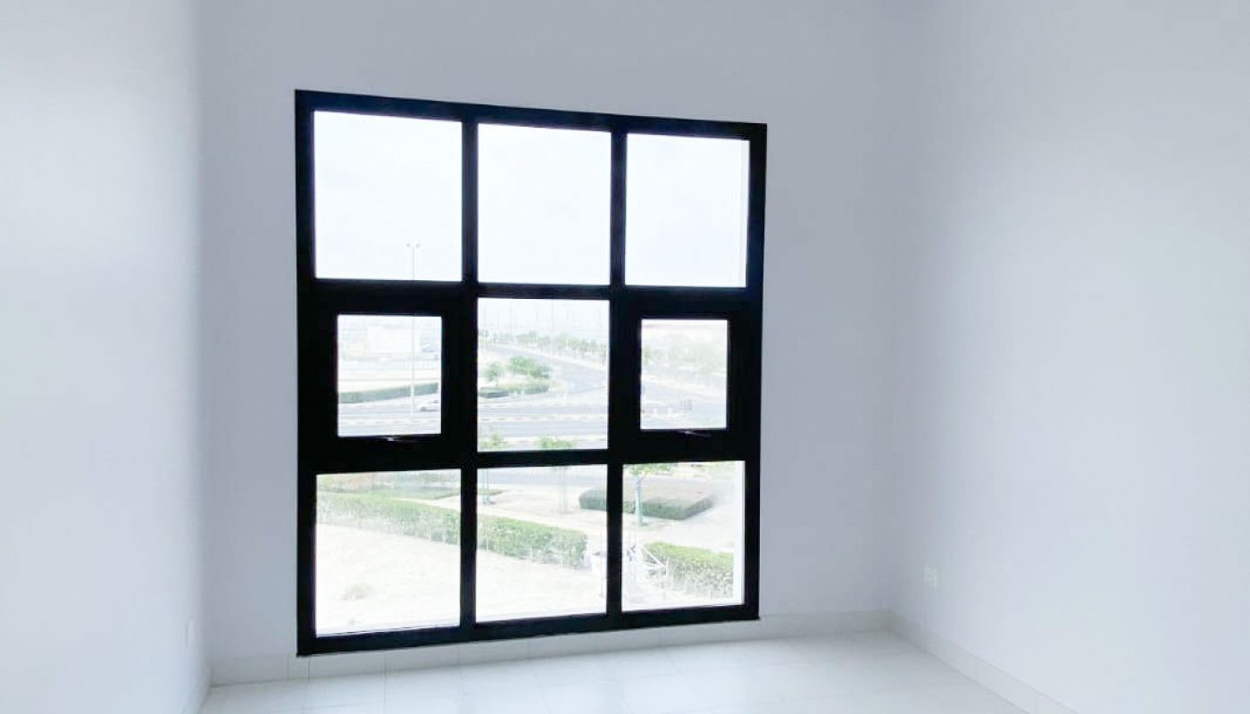 Empty white room with tiled floor, high ceiling, and a large black-framed window letting in natural light.