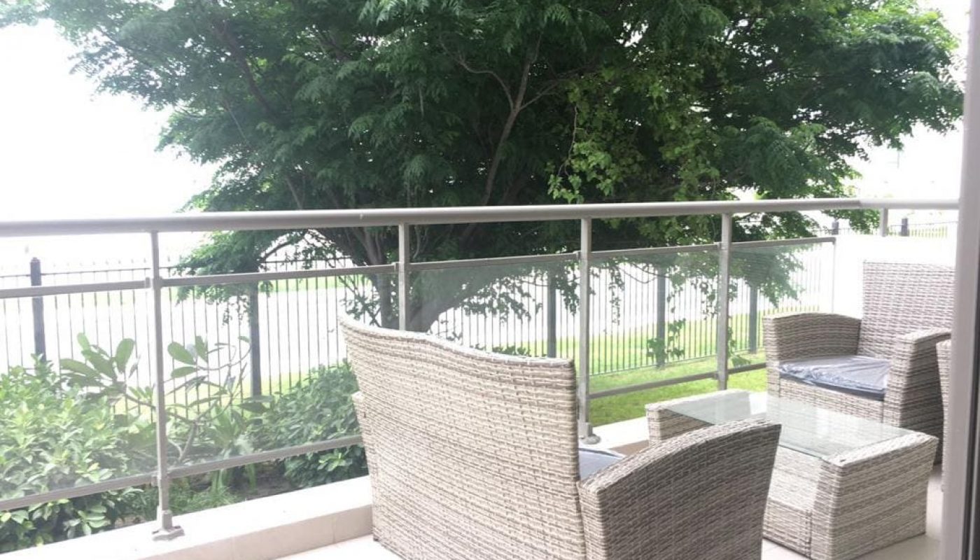 A fully furnished apartment with a balcony adorned with wicker furniture and overlooking a tree.