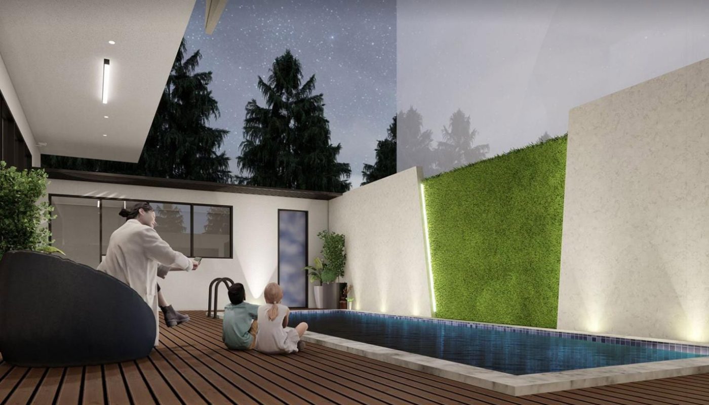 Two people sit near a rectangular pool on a wooden deck at night, surrounded by greenery and modern architecture.
