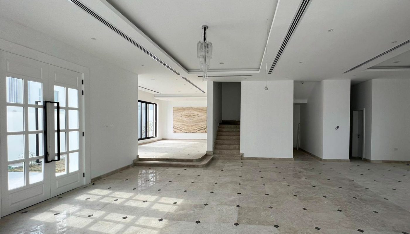 Spacious, empty room with tiled floor, white walls, French doors on the left, a chandelier, and a raised platform with stairs at the back.