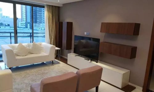 A furnished living room apartment with a flat screen tv and a view of the city, available for sale.
