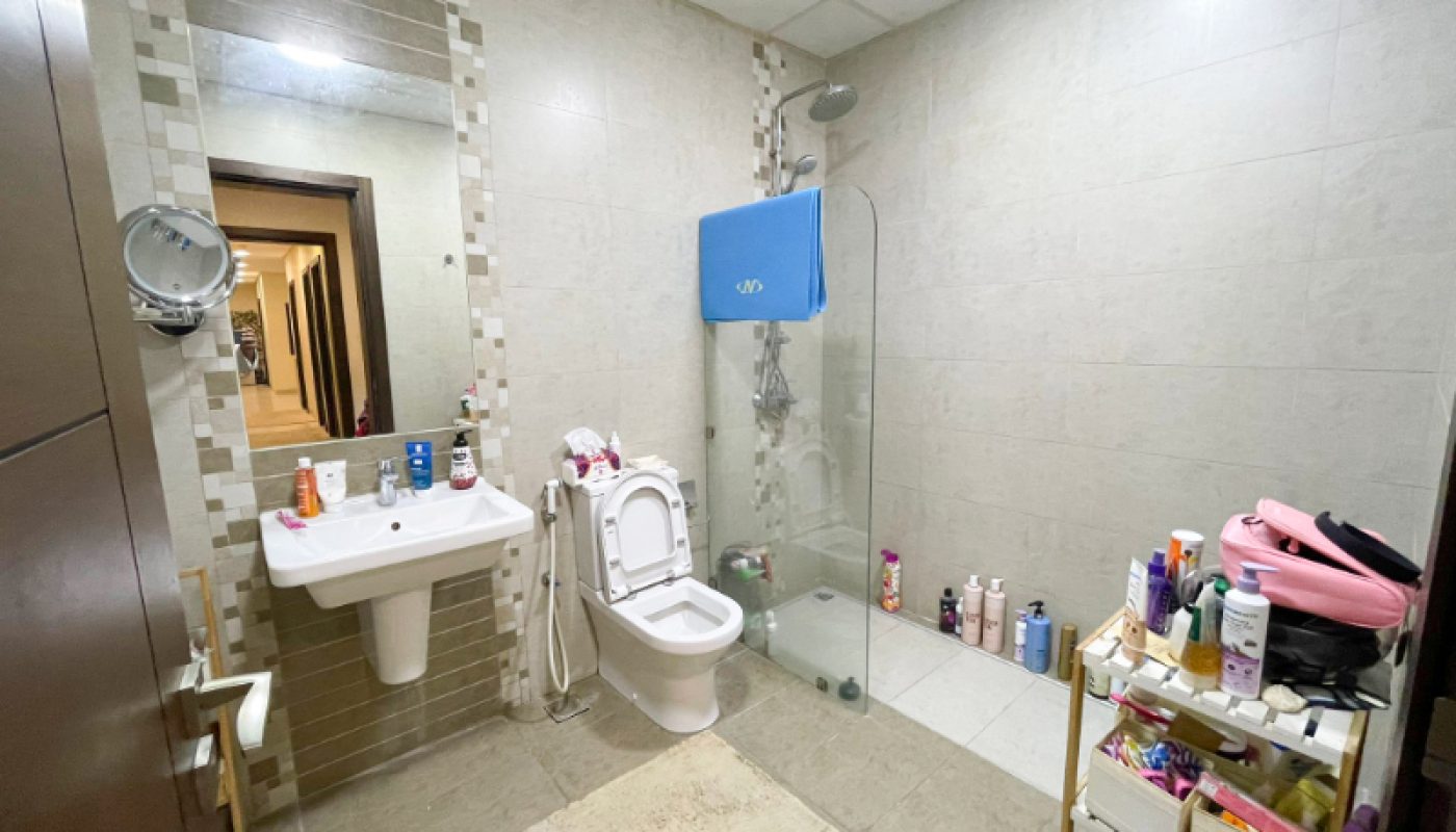 A bathroom with a sink, mirror, toilet, shower area, and shelves holding toiletries and personal care items.
