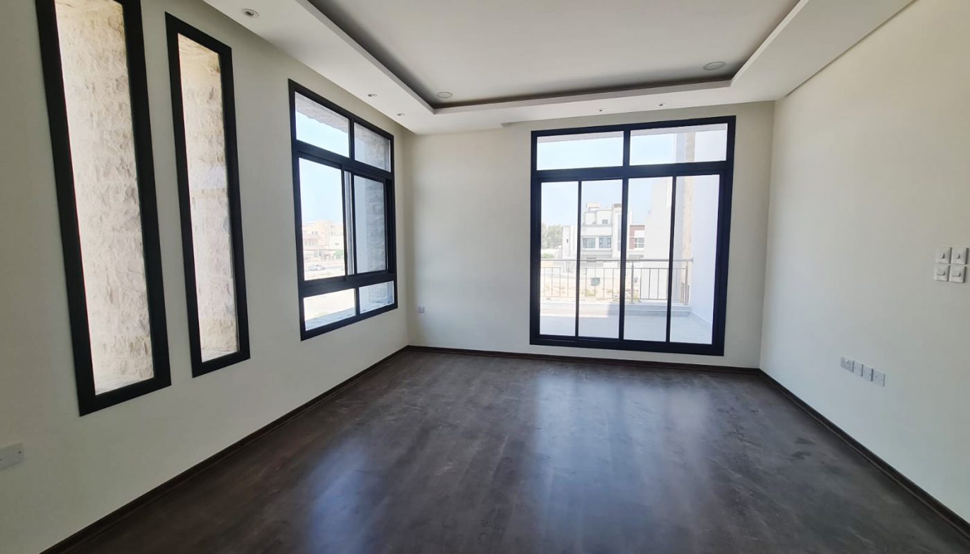 Empty room with large windows, dark wooden flooring, white walls, recessed ceiling lights, and a balcony view.