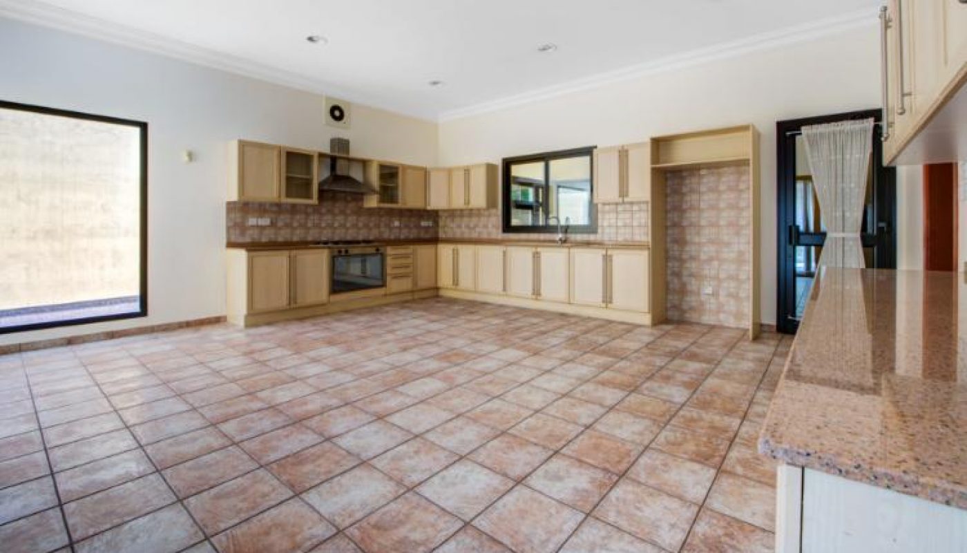Spacious kitchen with tiled floor, light wood cabinets, built-in oven, and large windows providing natural light.